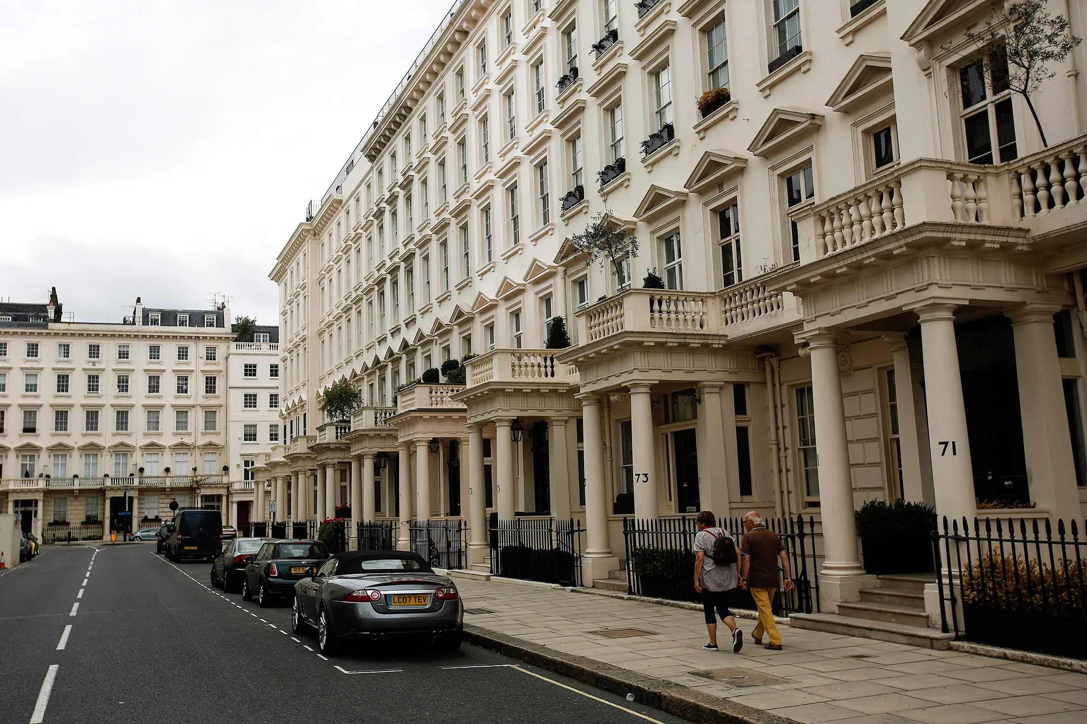 People walk past rows of luxury residential properties on Eaton Place in the Westminster district of London, U.K., on Monday, Aug. 10, 2015.
