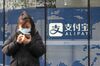 A pedestrian uses a smartphone in front of an Alipay sign outside an Ant Group Co. office building in Shanghai, China, on Thursday, Dec. 24, 2020.