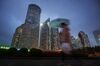 A pedestrian holding an umbrella walks past buildings illuminated at night in the Lujiazui district of Shanghai, China.
