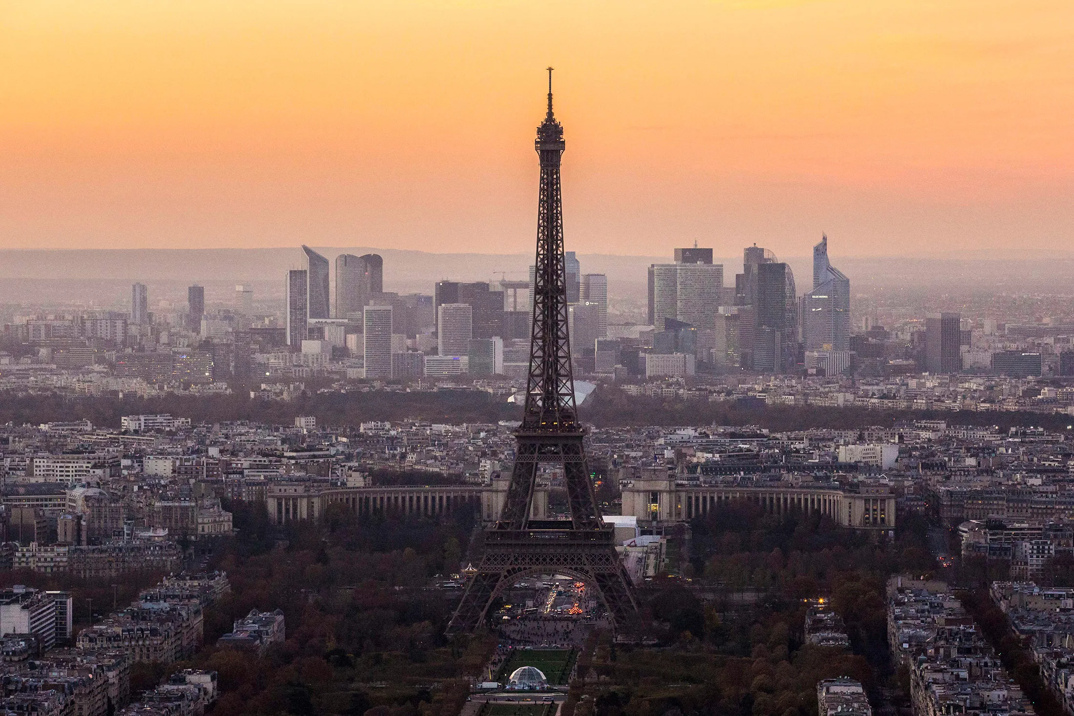 The Eiffel Tower stands above the city skyline as the sun sets over skyscrapers in La Defense business district in Paris,.
