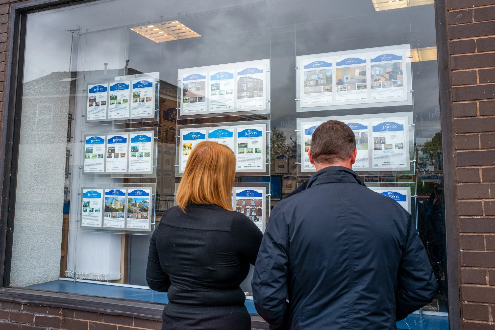 Pedestrians look at properties in the window of an estate agents in Stalybridge, U.K.