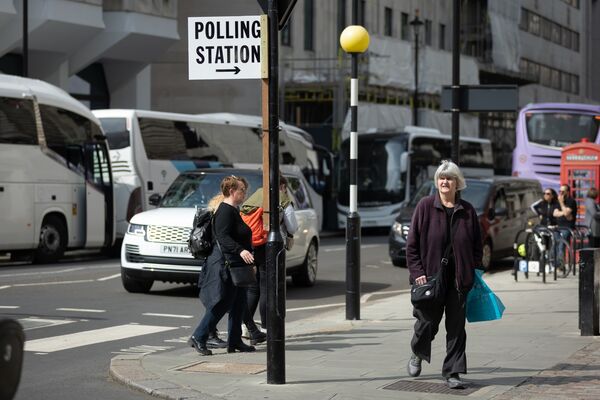 People walk by a sign pointing to a polling station ahead of