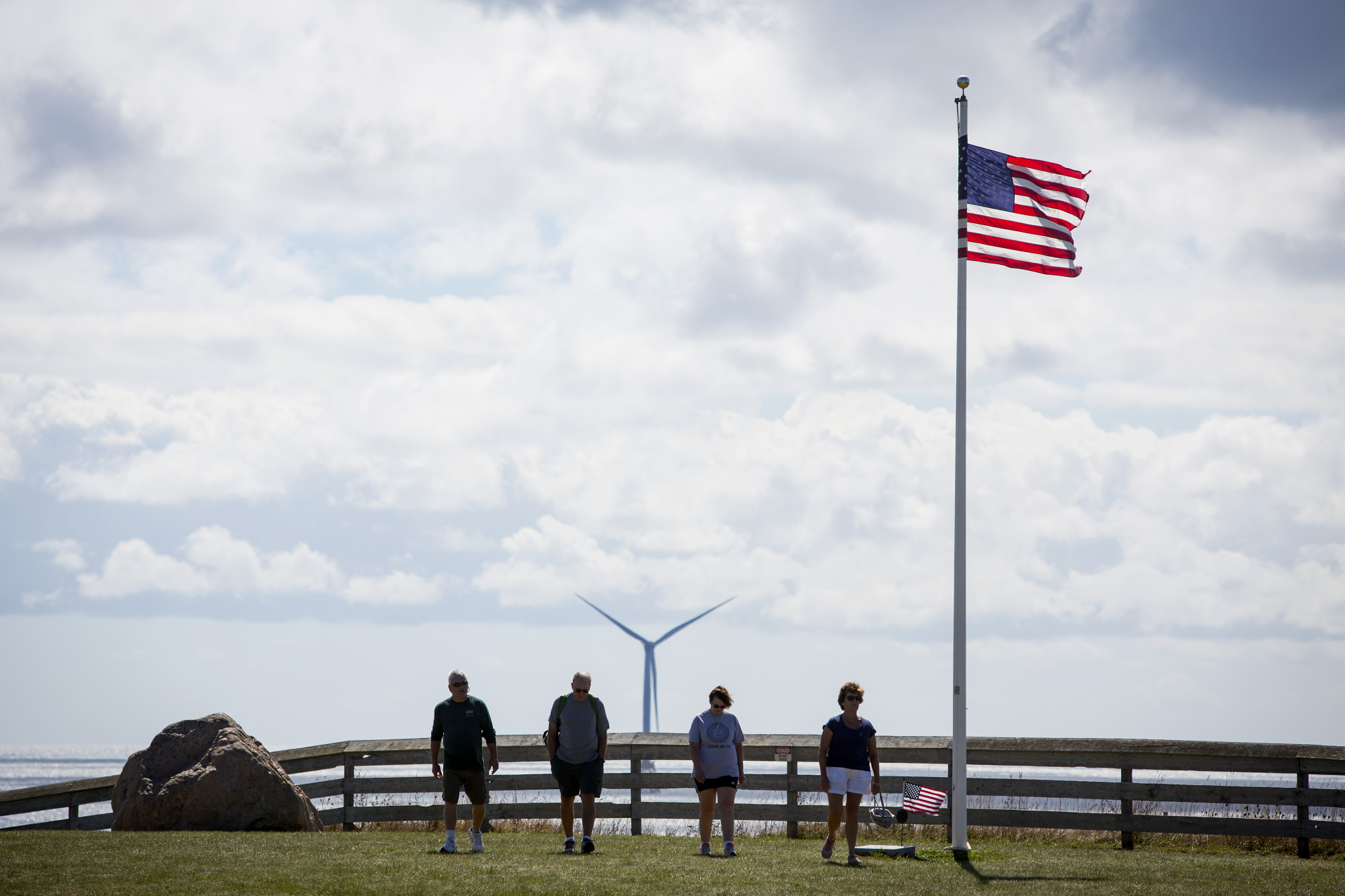 Tourists walk past an American flag near an Ørsted wind turbine off Block Island, Rhode Island