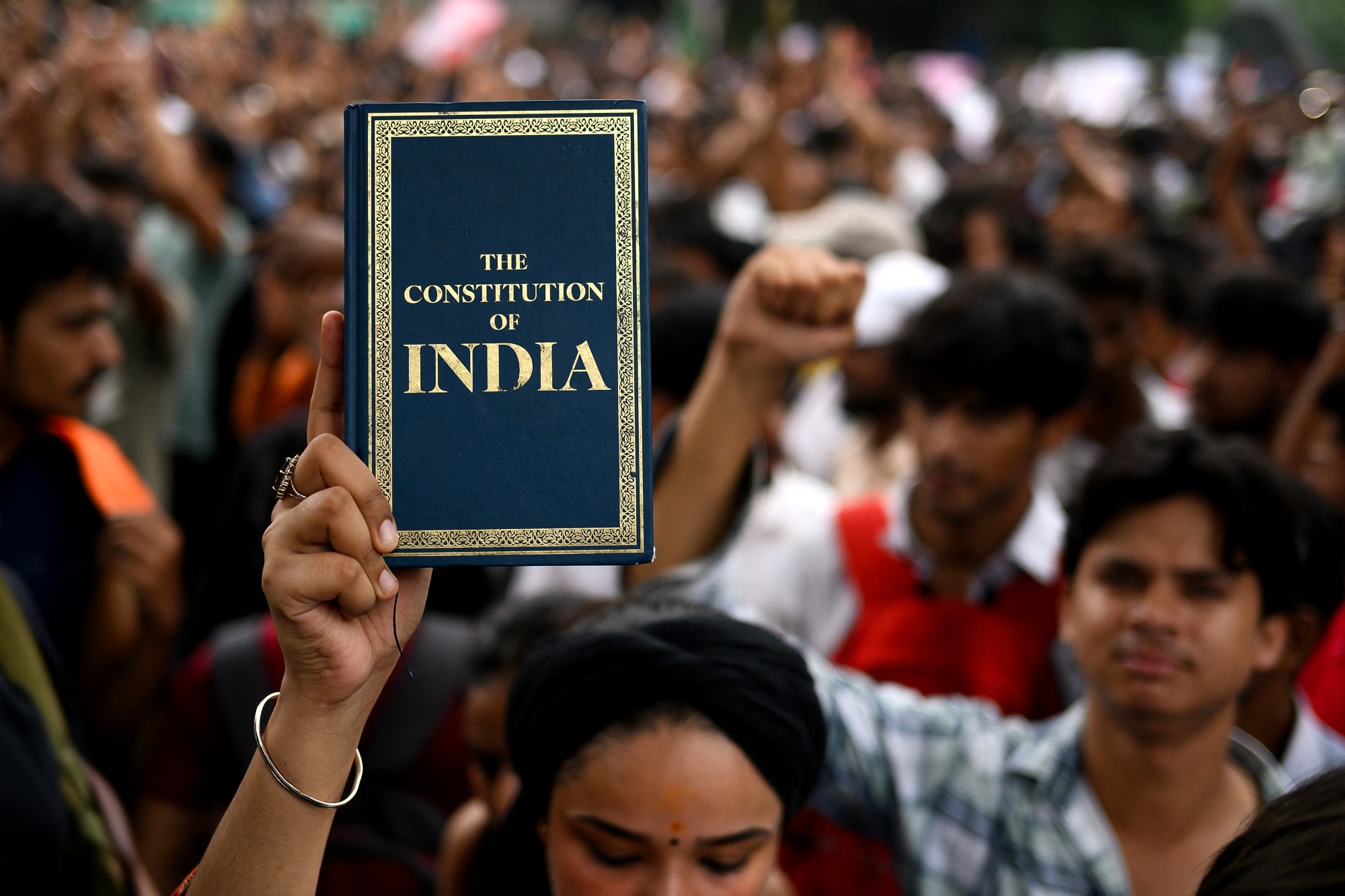 An activist and supporter of the Cockroach Janta Party (CJP) holds a copy of 'The Constitution of India' during a protest demanding the resignation of India's Education Minister Dharmendra Pradhan over alleged NEET examination irregularities in New Delhi on July 20, 2026. (Photo by Manan VATSYAYANA / AFP via Getty Images) Photographer: MANAN VATSYAYANA/AFP