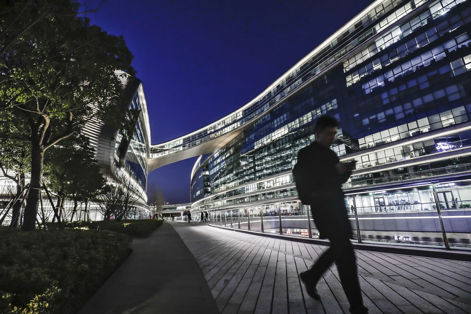 A pedestrian walks past the illuminated Sky Soho building in&nbsp;Shanghai.