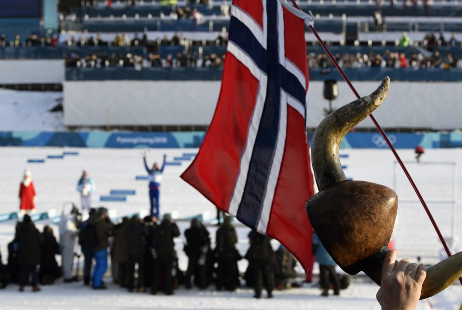 A spectator raises Norway's flag and a horned helmet as gold medalist Marit Bjoergen celebrates on the podium.