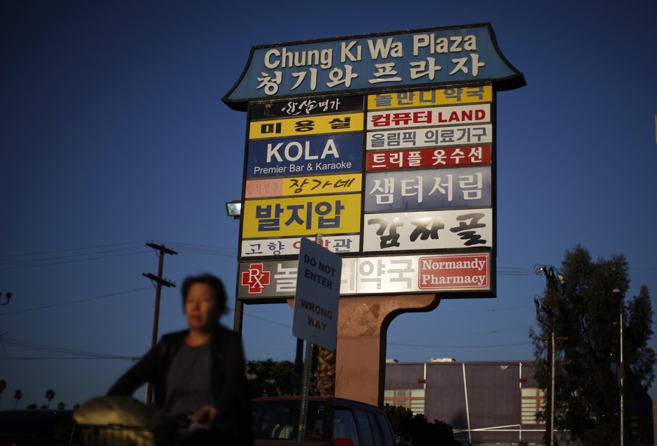 A woman cycles past a sign in Korean in the Koreatown area of Los Angeles, California. 