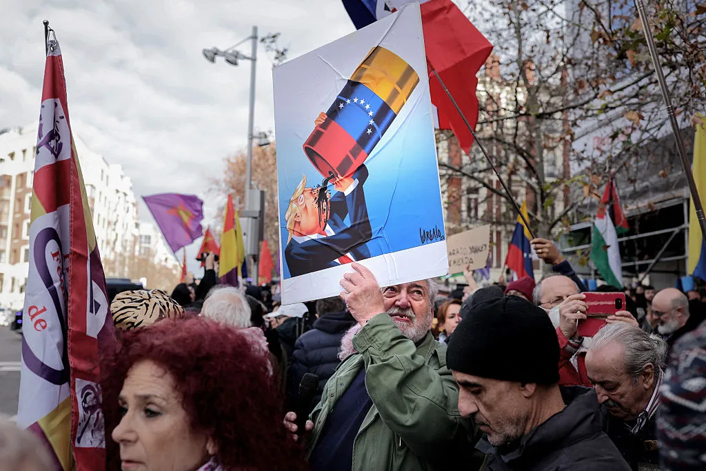A Madrid protestor holds a caricature of Donald Trump drinking from a Venezuelan oil barrel by Portuguese cartoonist Vasco Gargalo.