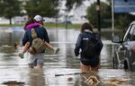 Don Noel carries his daughter Alexis, 8, with his wife Lauren, right as they walk through a flooded roadway in New Orleans.