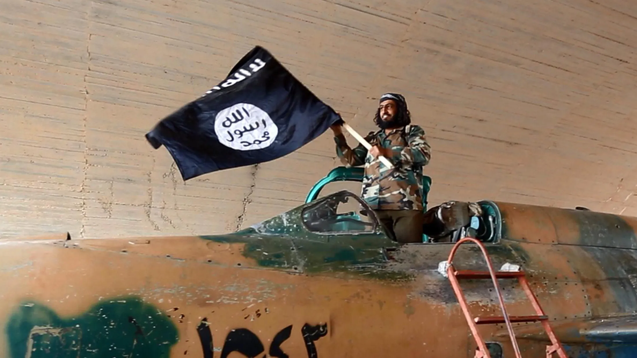 An Islamic State fighter waves a flag while standing on a captured government fighter jet in Raqqa, Syria, 2015.
