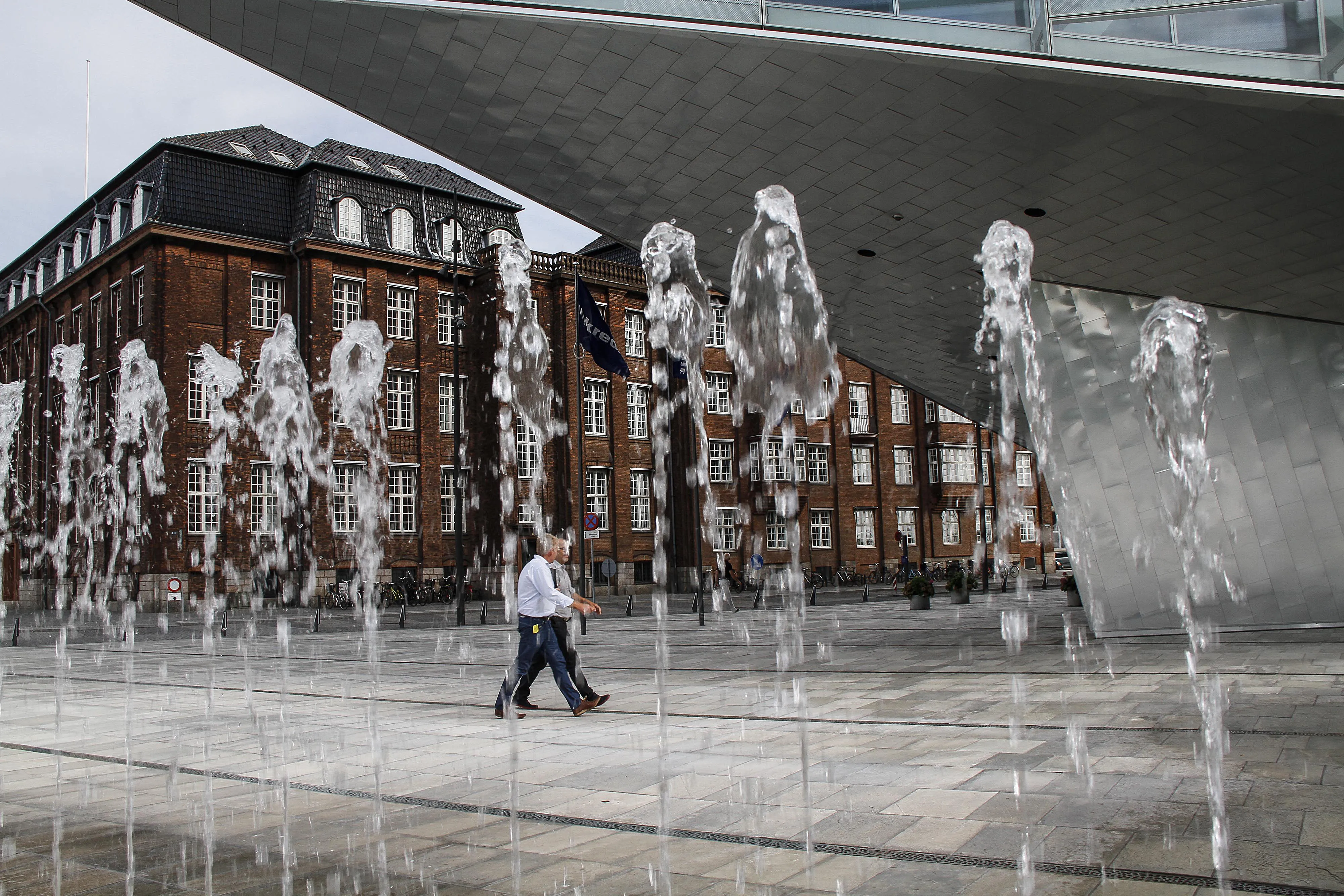 Pedestrians pass a water fountain outside the offices of Nykredit Realkredit A/S bank in Copenhagen.