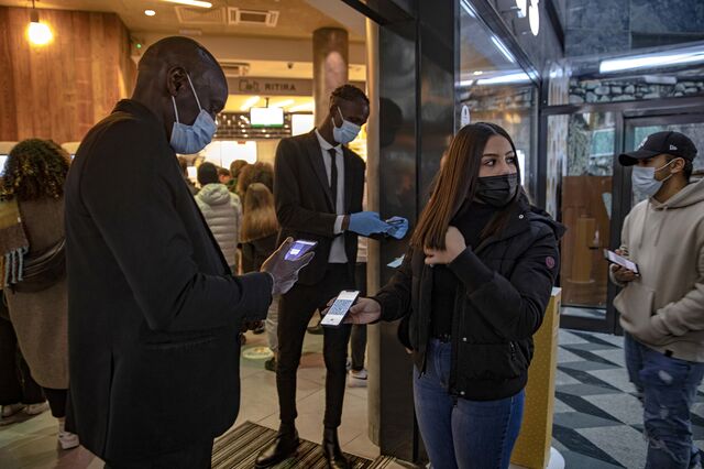 A worker checks a customer's digital "green pass" at the entrance to a fast food restaurant in Milan, Italy, on Saturday, Nov. 27, 2021. Prime Minister Mario Draghi's government has approved new curbs targeting mainly unvaccinated people in a bid to shield Italy from a surge of coronavirus cases elsewhere in Europe.
