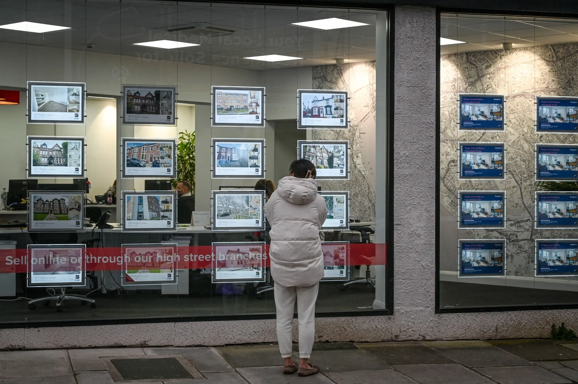 A pedestrian looks at properties in the window of an estate agent shop in the Mossley Hill area of Liverpool.