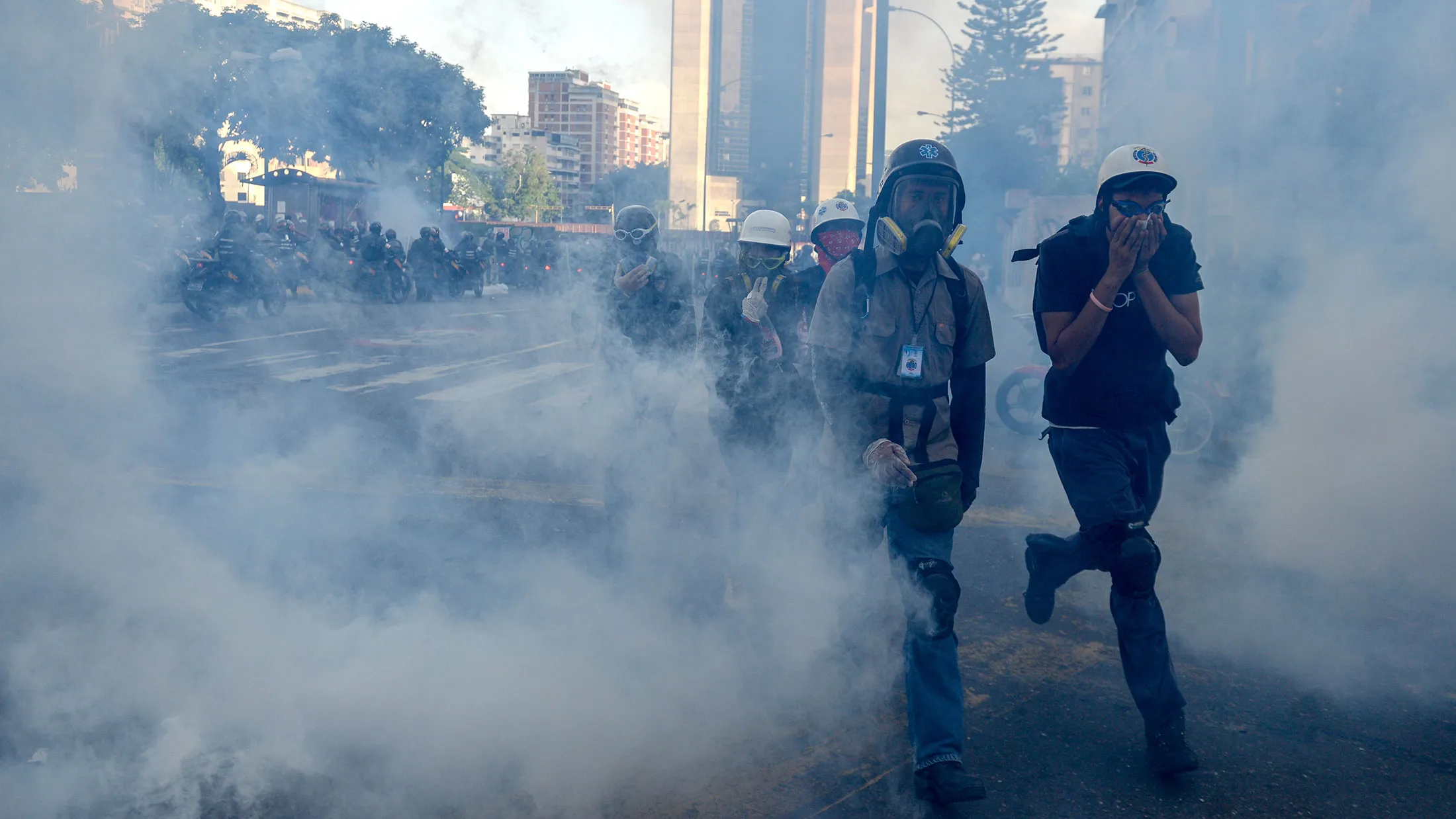 Volunteer medics cross a cloud of tear gas as opposition activists demonstrating against the government of Venezuelan President Nicolas Maduro clash with riot police in Caracas on June 26, 2017.

