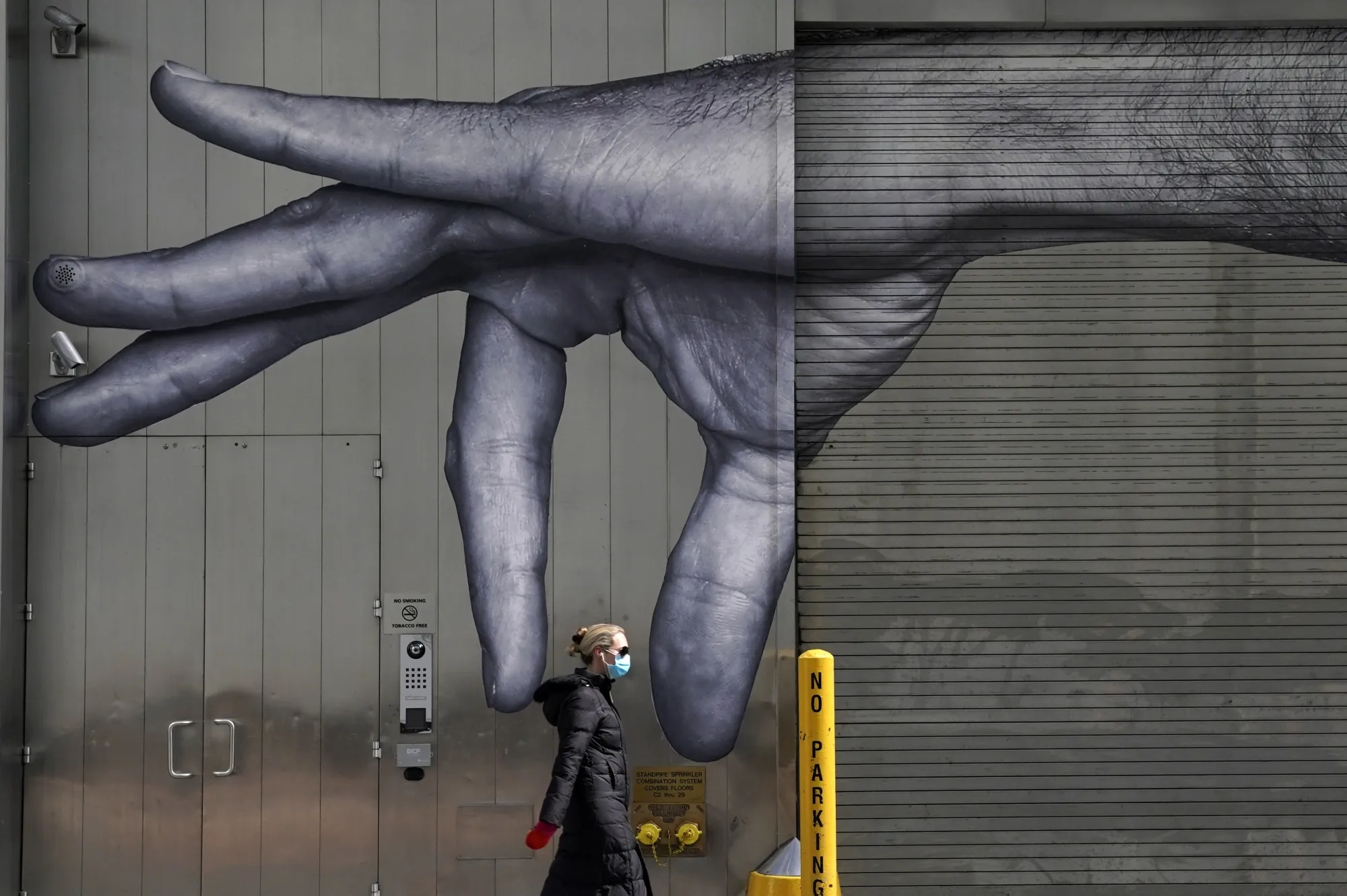 A woman in a mask walks past a mural in Midtown New York City, April 22.