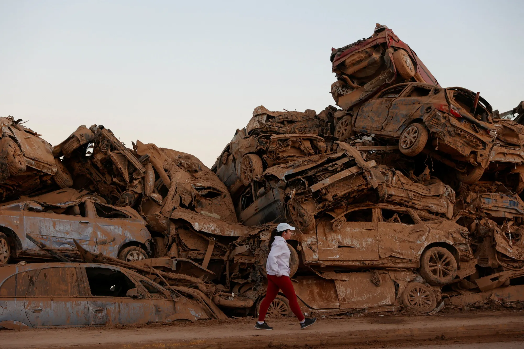 Nearly a month after severe flooding, a person walks past a field where water-ravaged cars are piled up in&nbsp;Valencia, Spain on Nov. 28
