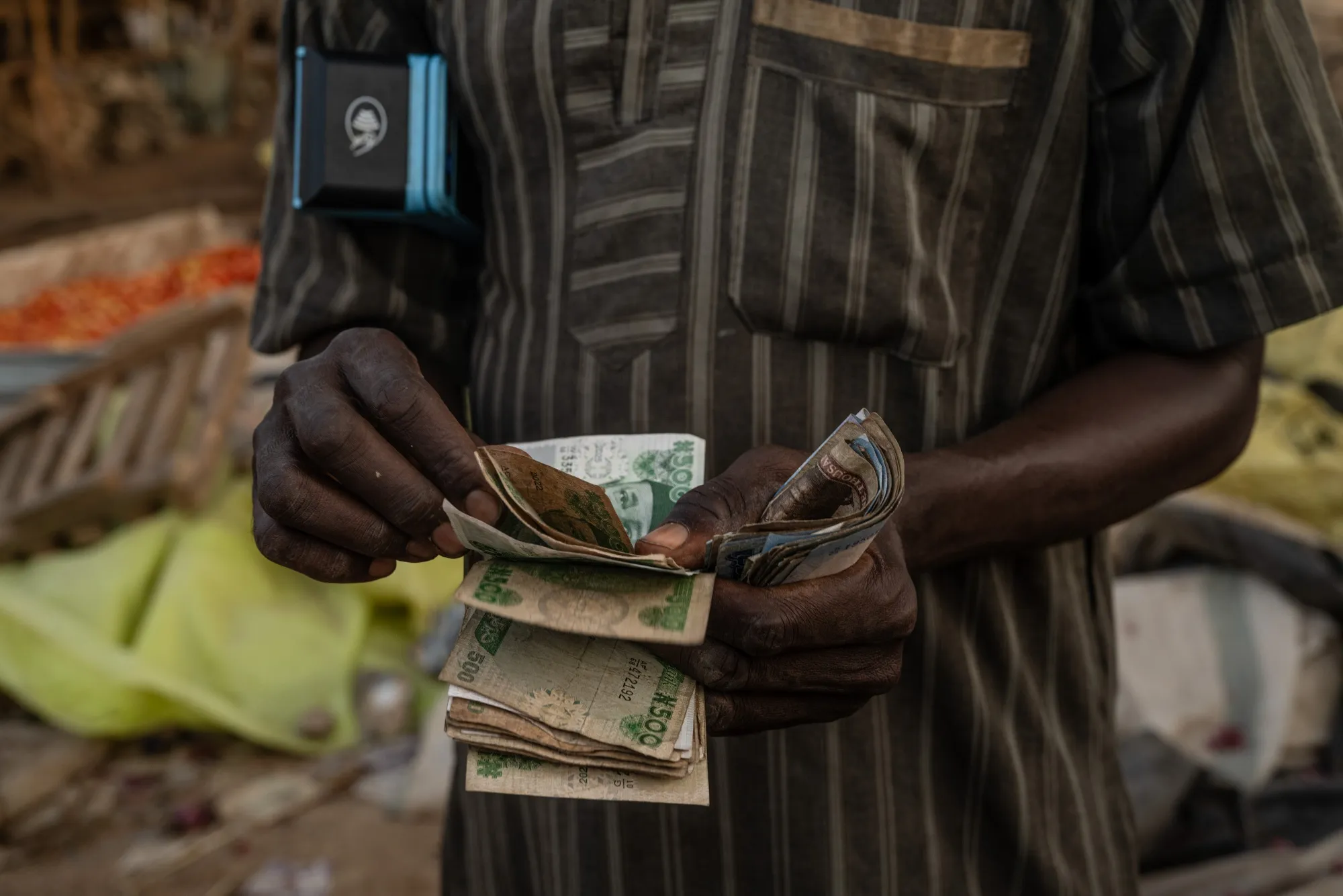 A seller holds an electronic payment terminal while counting Nigerian naira banknotes at a market in Abuja, Nigeria.