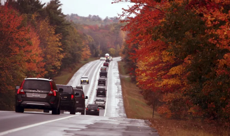 Cars drive through a scenic roadway in Maine during the fall season.