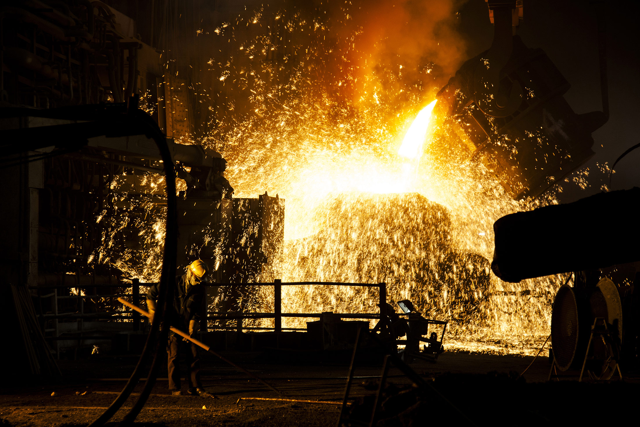 A worker works while sparks fly as molten steel is poured from a ladle at an arc furnace in a steel plant in Chhattisgargh.

