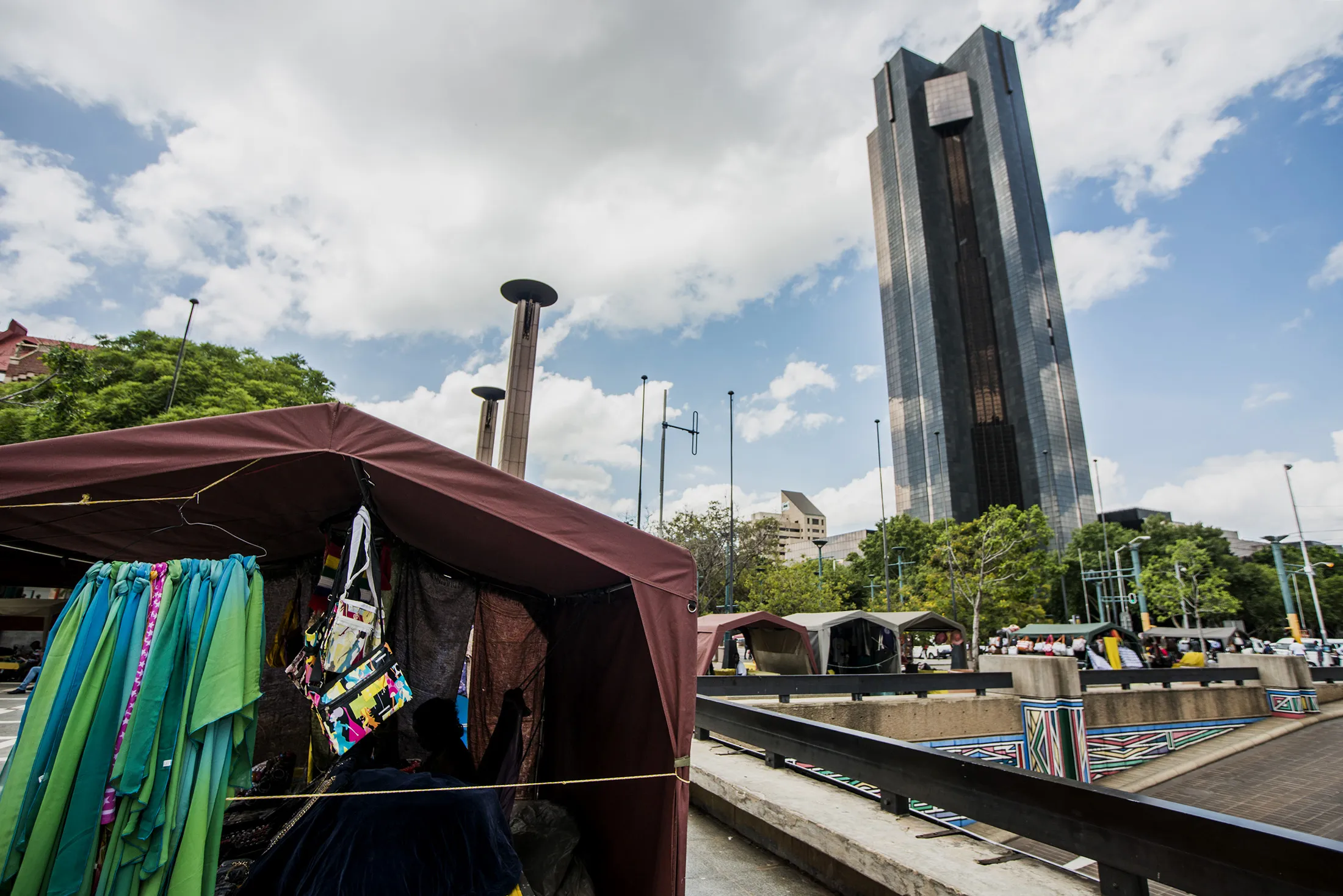 Street hawkers sell their wares to passing pedestrians on a road near the headquarters of the South African Reserve Bank, right, in Pretoria, South Africa.
