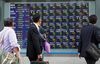 Pedestrians look at an electronic stock board outside a securities firm in Tokyo, Japan, on Friday, April 5, 2013. Japanese stocks surged, with the Nikkei 225 Stock Average capping the biggest three-day rally in two years, after Haruhiko Kuroda announced unprecedented stimulus in his first policy meeting as Bank of Japan governor.