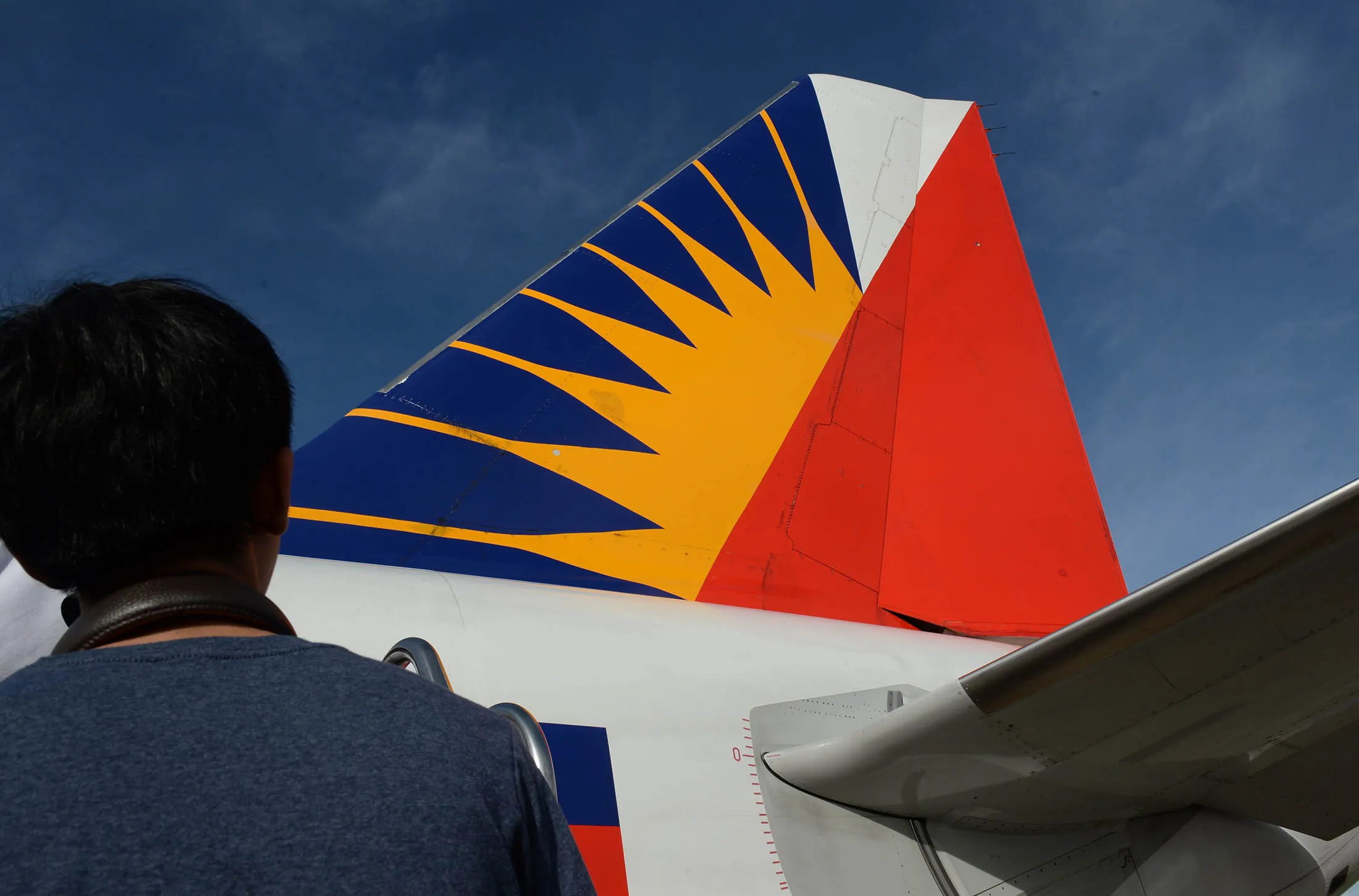 A passenger looks at the tail of a Philippine Airlines aircraft.
