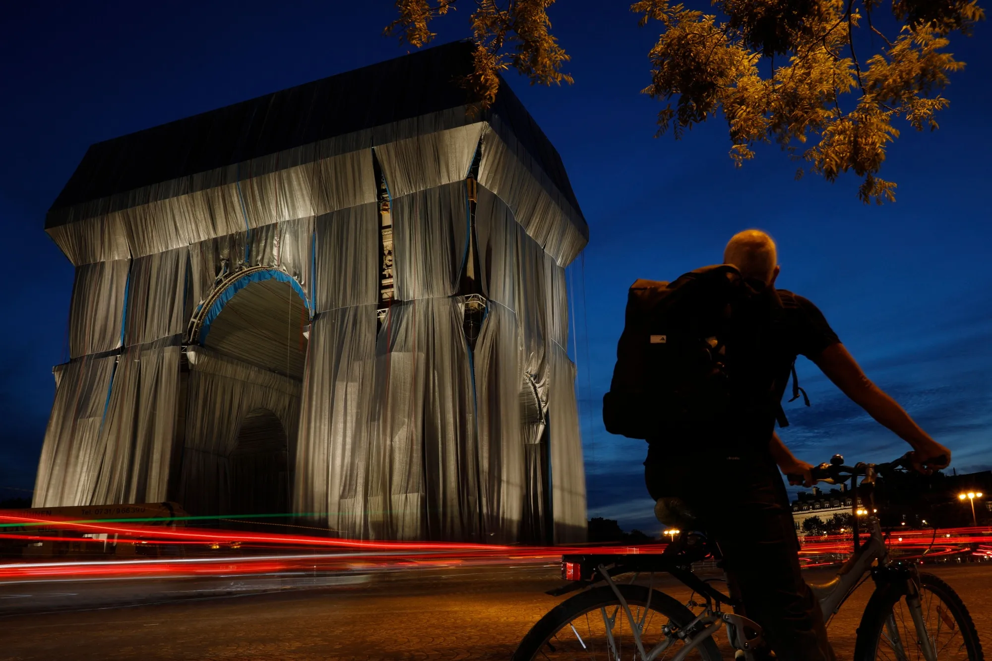 A cyclist looks at the Arc de Triomphe, in Paris, wrapped in silver-blue fabric as it was designed by the late artists Christo and Jeanne-Claude.