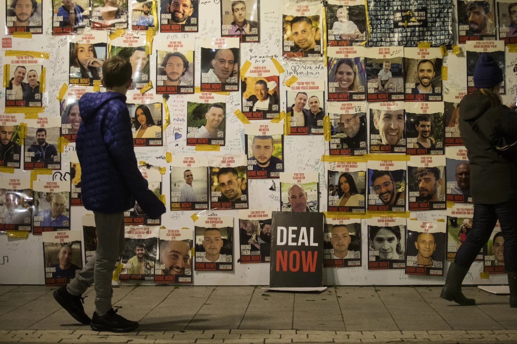 People walk by a wall with photos of hostages held in Gaza by Hamas in Tel Aviv, Israel.