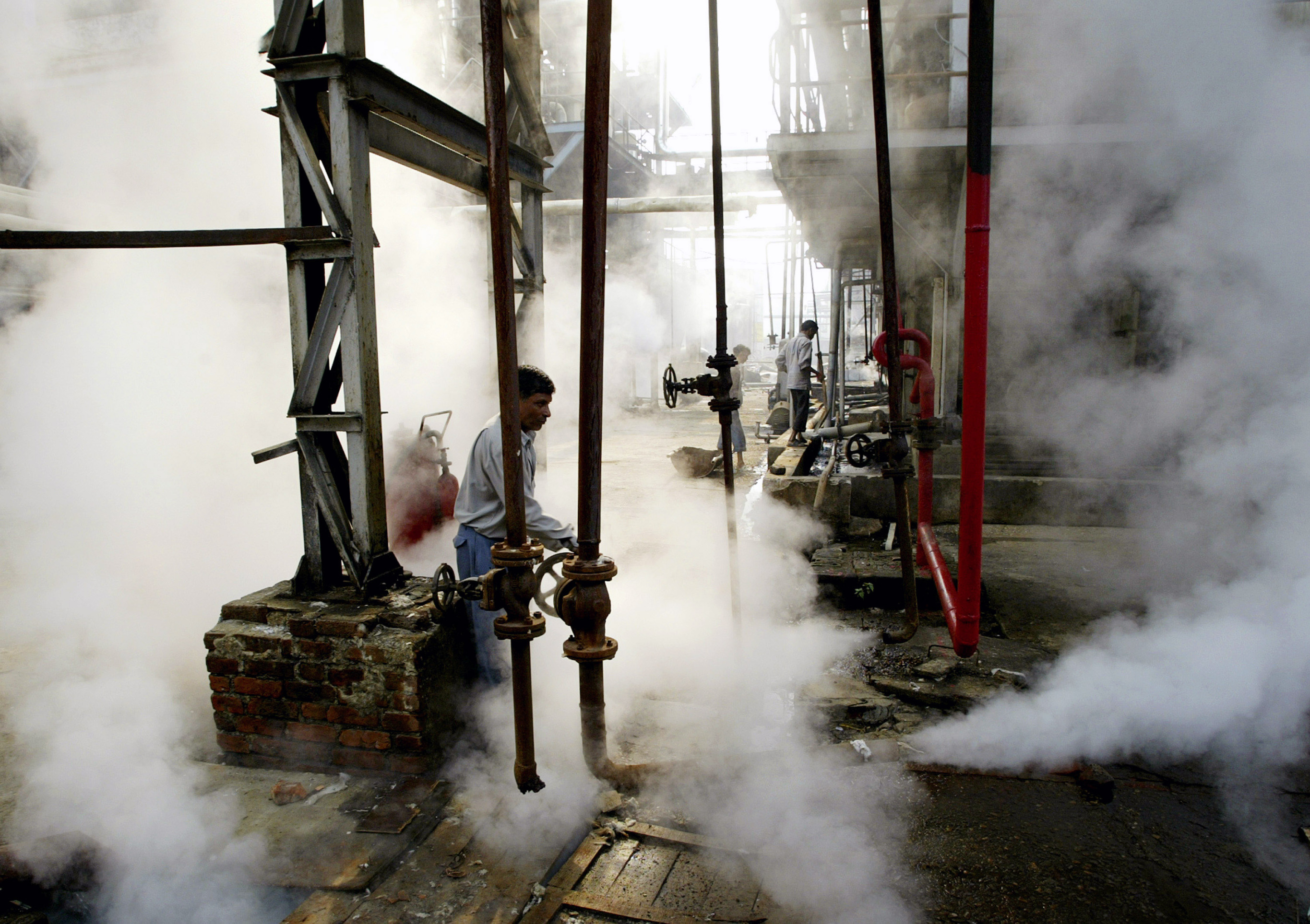 A worker operates a valve to release steam at a distillery in India.