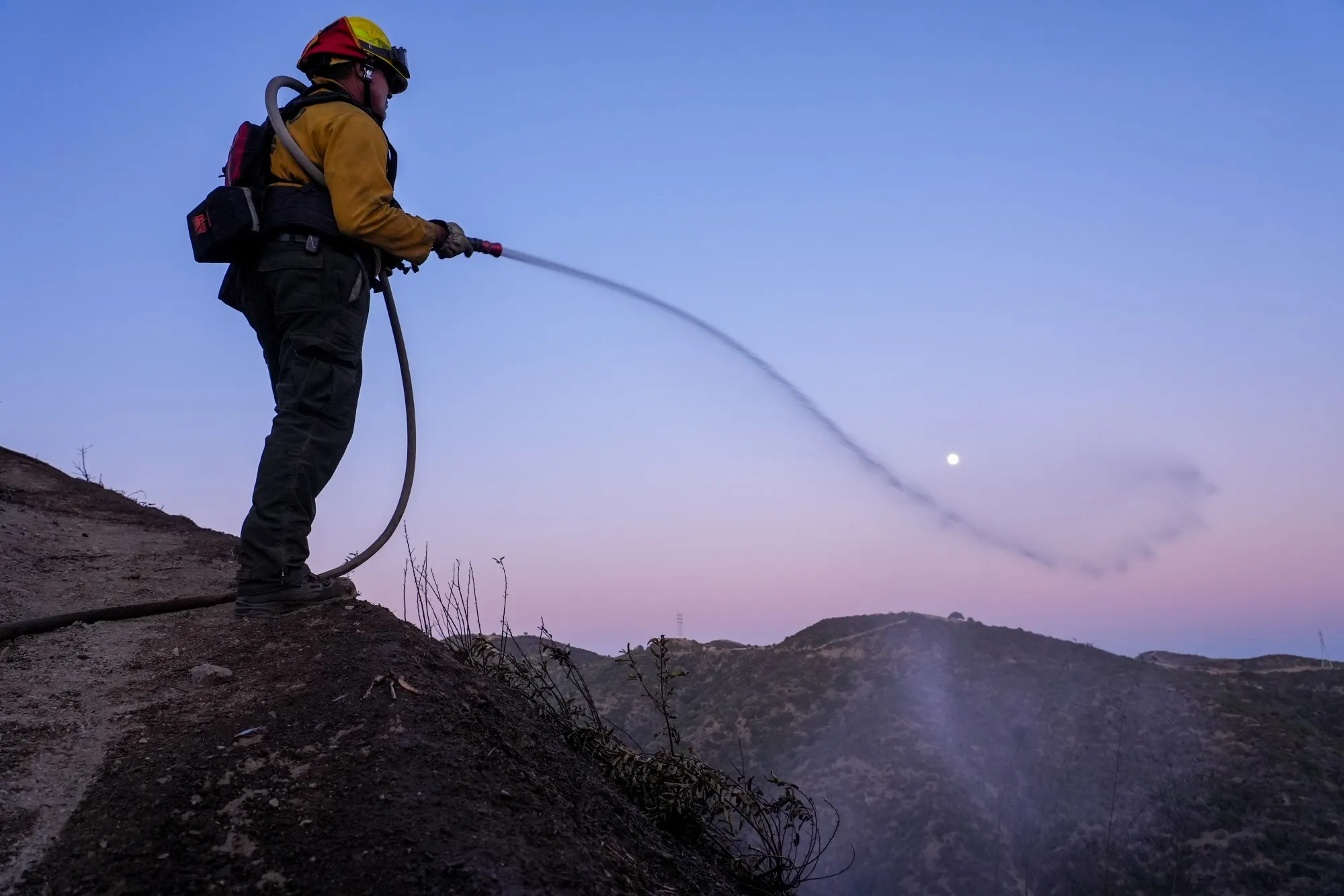 A firefighter&nbsp;sprays water over a hillside in the aftermath of the Palisades Fire in the Mandeville Canyon area of Los Angeles, on Jan. 12.