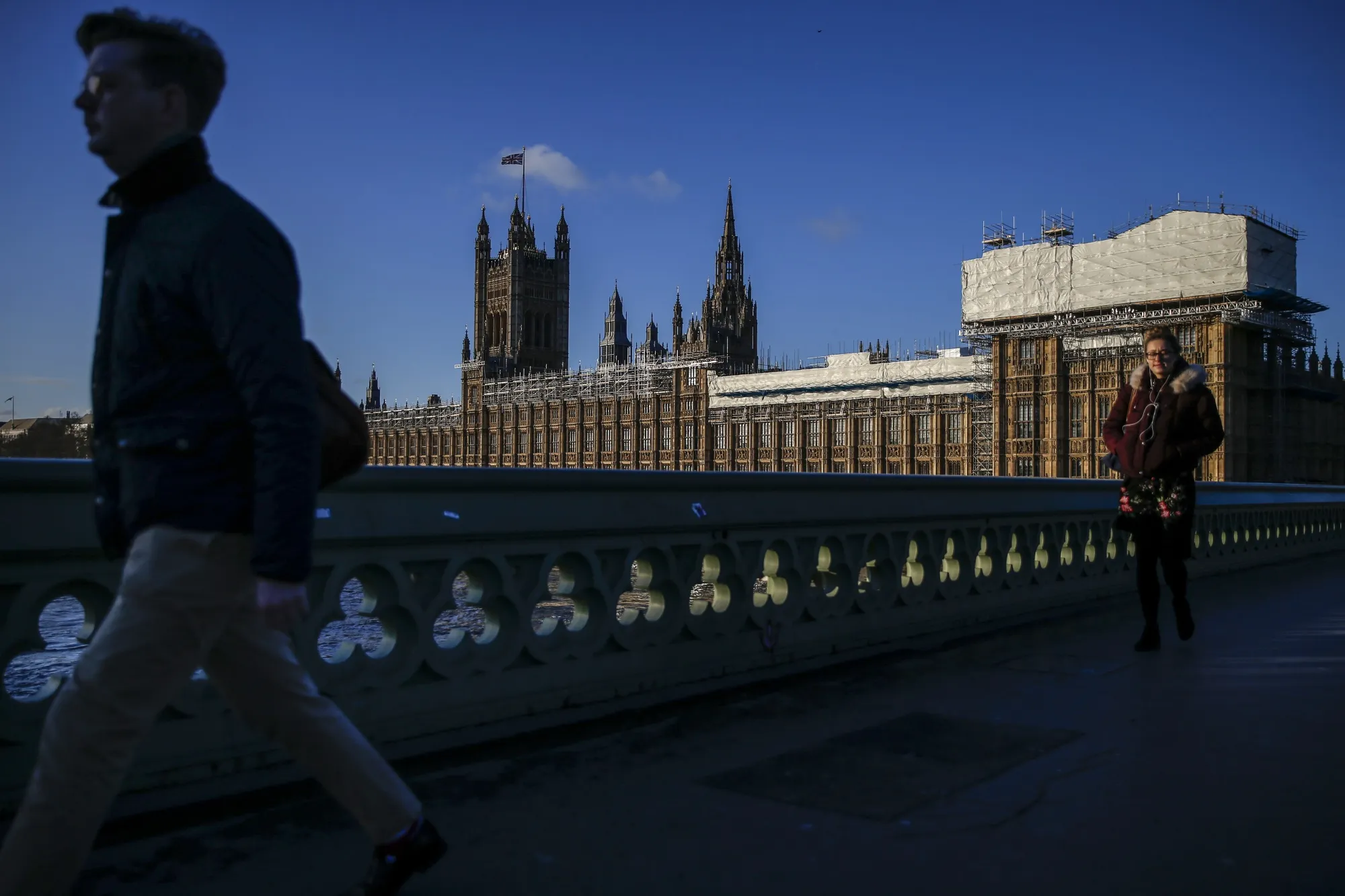Pedestrians cross Westminster Bridge in view of the Houses of Parliament in London.