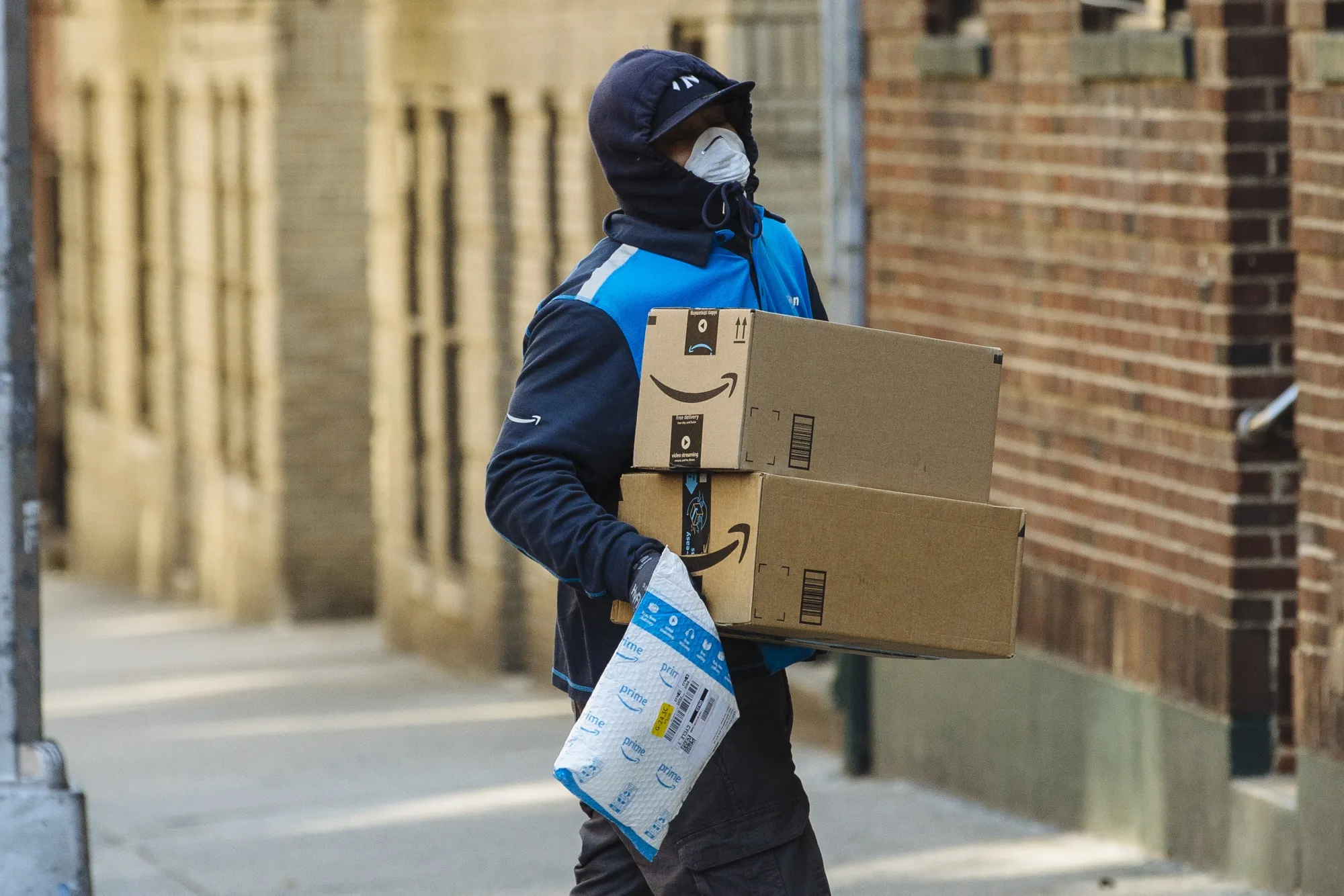 A worker wearing a protective mask and gloves carries Amazon&nbsp;boxes during a delivery in New York on March 26.