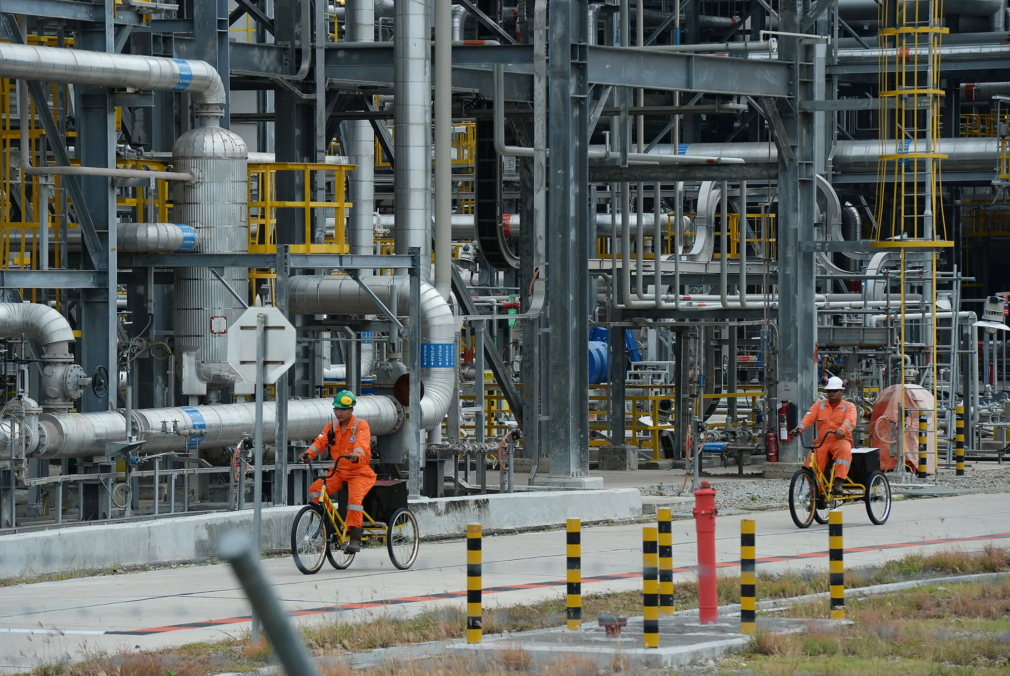Workers ride bicycles past oil and gas processing infrastructure at the Exxon Mobil Corp. Banyu Urip Central Processing Facility in the Cepu block of Bojonegoro, East Java, Indonesia, on Dec. 8, 2016.
