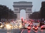 Vehicles sit at traffic lights as the Arc de Triomphe stands beyond in Paris.