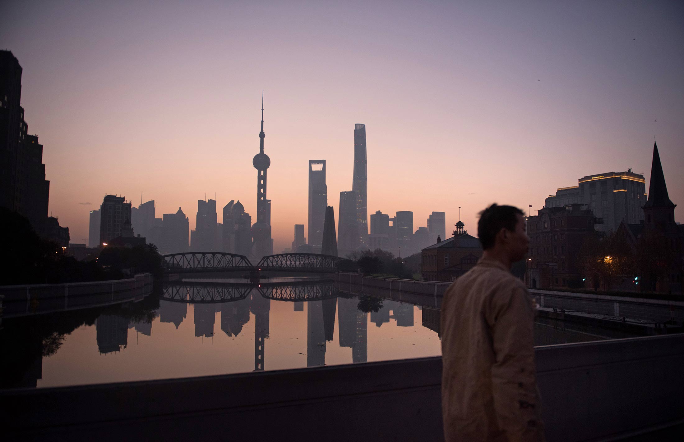 A man walks over a bridge in front of the skyline of the Lujiazui Financial District in Pudong in Shanghai at dawn on Dec. 1, 2015.
