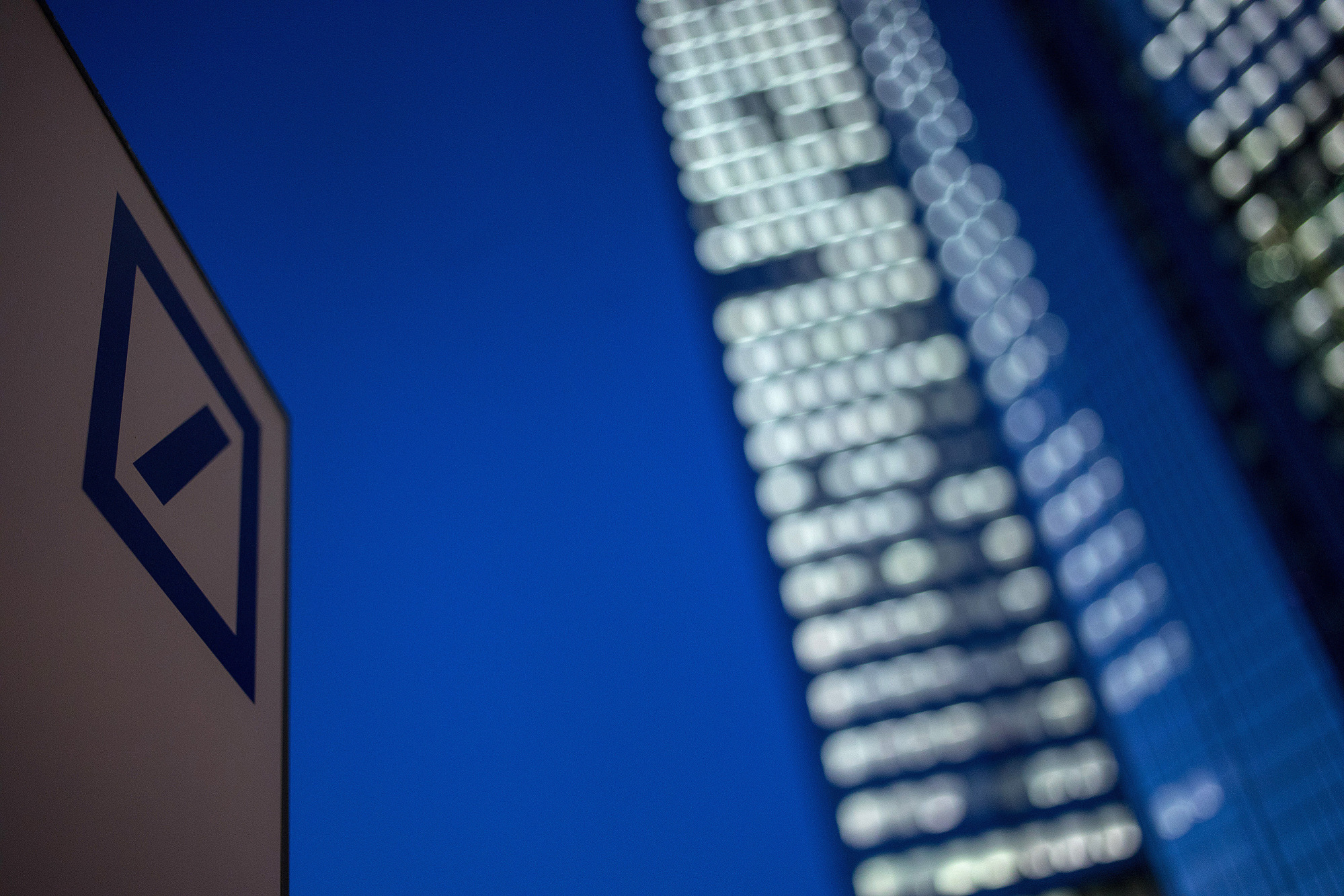 A logo sits on a sign outside the Deutsche Bank AG headquarters skyscraper buildings at night in Frankfurt, Germany.