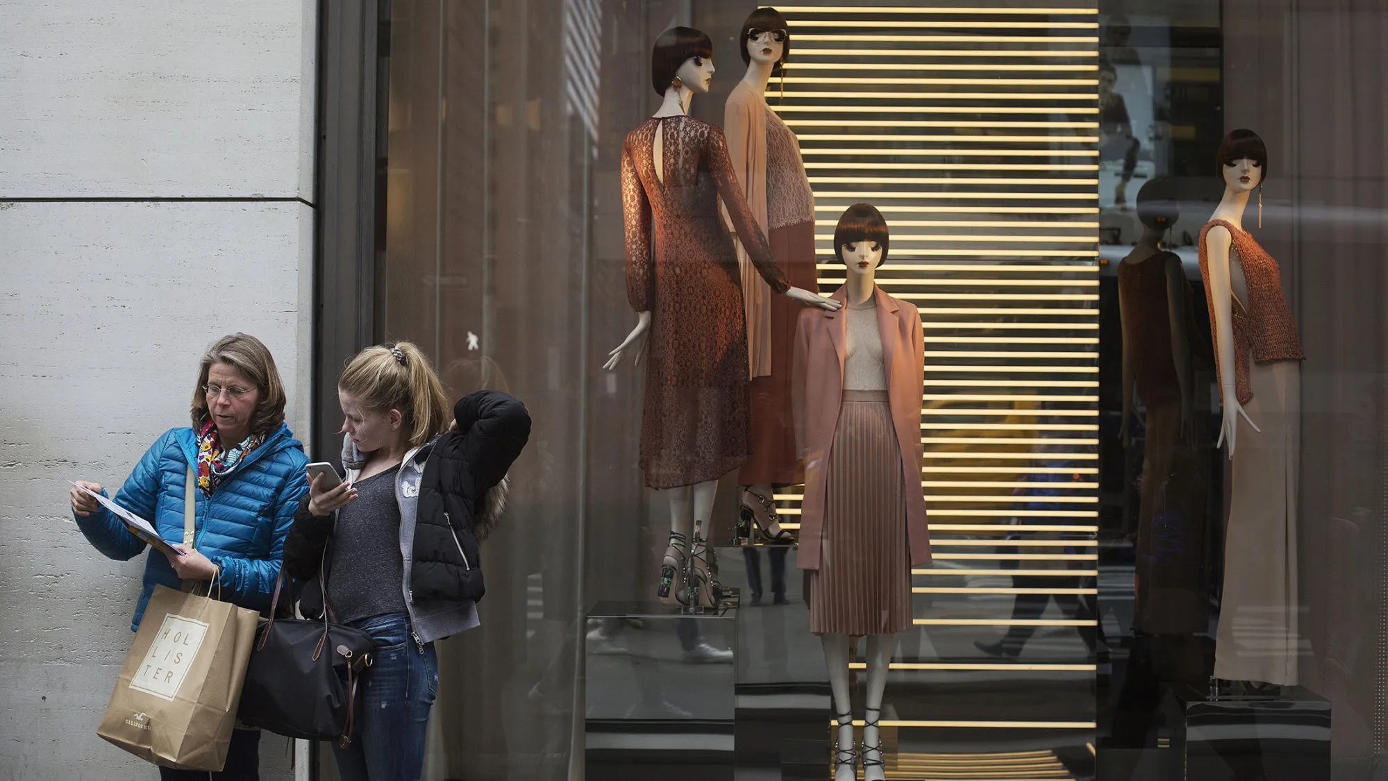 Shoppers stand in front of a store window displaying mannequins on Fifth Avenue in New York.