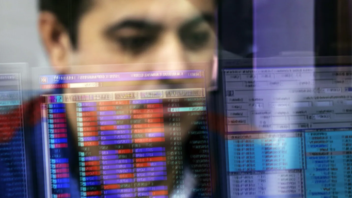 An employee is reflected in a glass panel as he monitors securities on a computer monitor at a brokerage firm in Mumbai, India, on Tuesday, Aug. 25, 2015. Indian stocks advanced in volatile trading a day after the benchmark gauge plunged the most in six years, as banks helped counter declines in software exporters.
