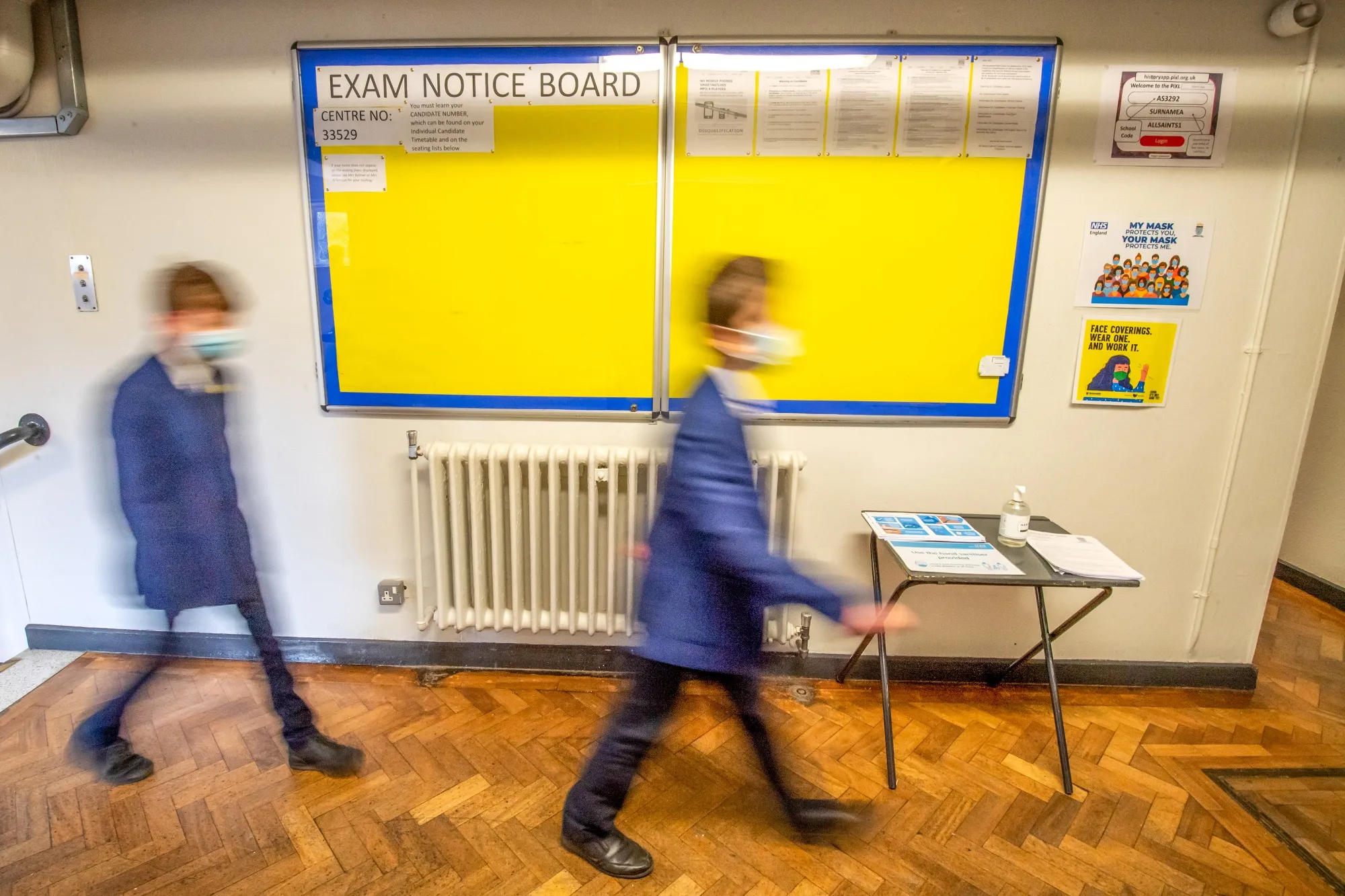 Pupils wearing face masks walk past an empty exams notice board at a school in Dukinfield, U.K..