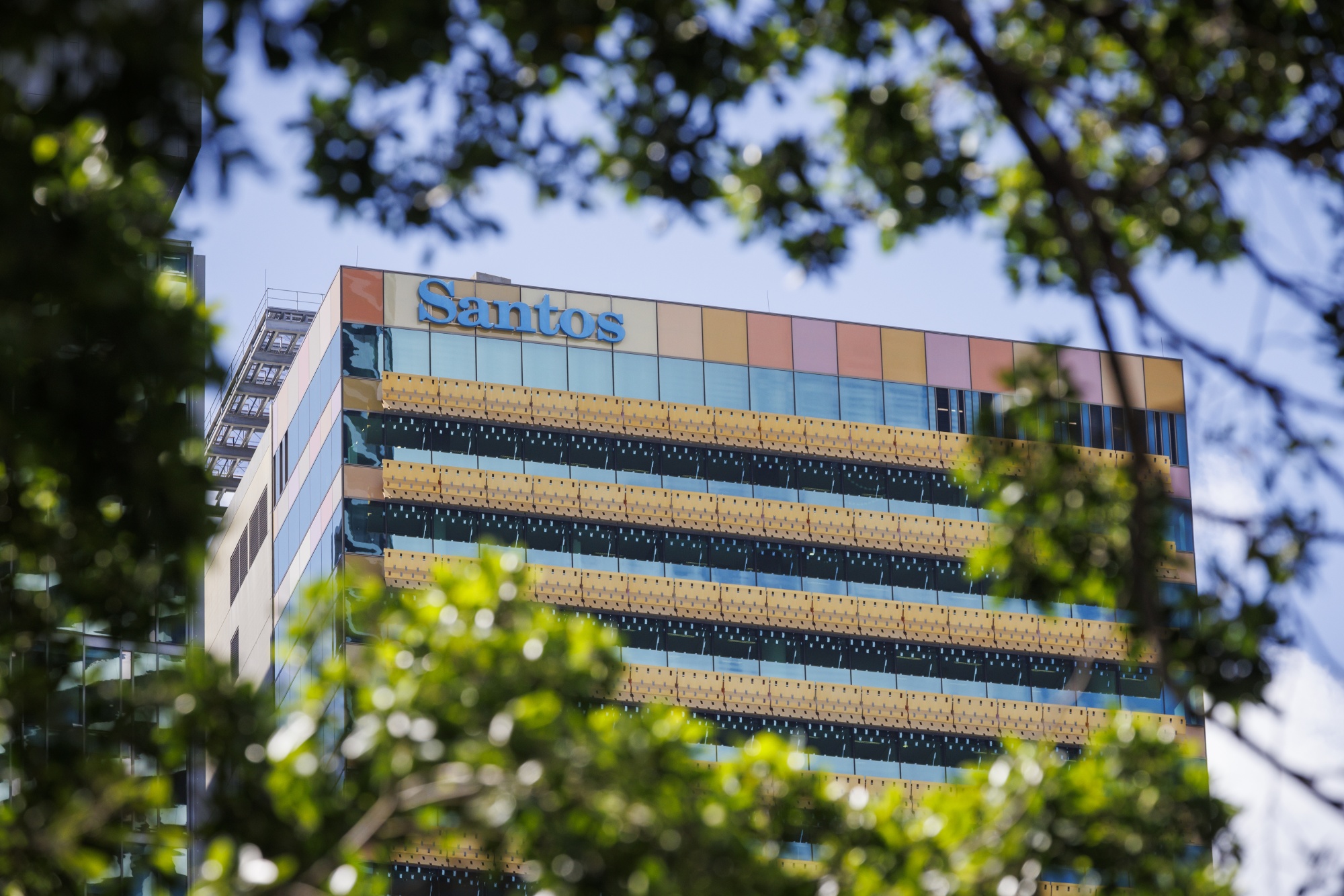 The Santos Ltd. Logo atop Santos Place building, which houses the company's office, in Brisbane, Australia, on Monday, Dec. 11, 2023. Woodside Energy Group Ltd.’s hopes of a tie-up with Santos to create Asia’s dominant liquefied natural gas exporter face a potential hurdle over the valuation of a target whose shares recently fell to an eight-month low. Photographer: Ian Waldie/Bloomberg