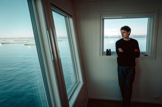 Gustav Magnar Witzøe standing inside of a room, looking out towards the water while visiting Salmar's largest fish farm where he used to work shifts in his 20's.