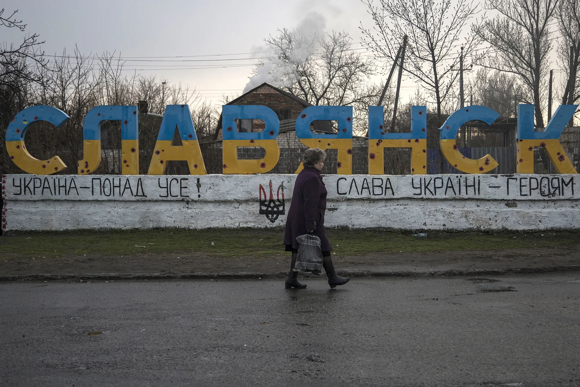 A woman passes in front of the Slaviansk sign that is full of holes&nbsp;caused by&nbsp;clashes between the Ukrainian government and rebel groups&nbsp;in Slaviansk, Ukraine.