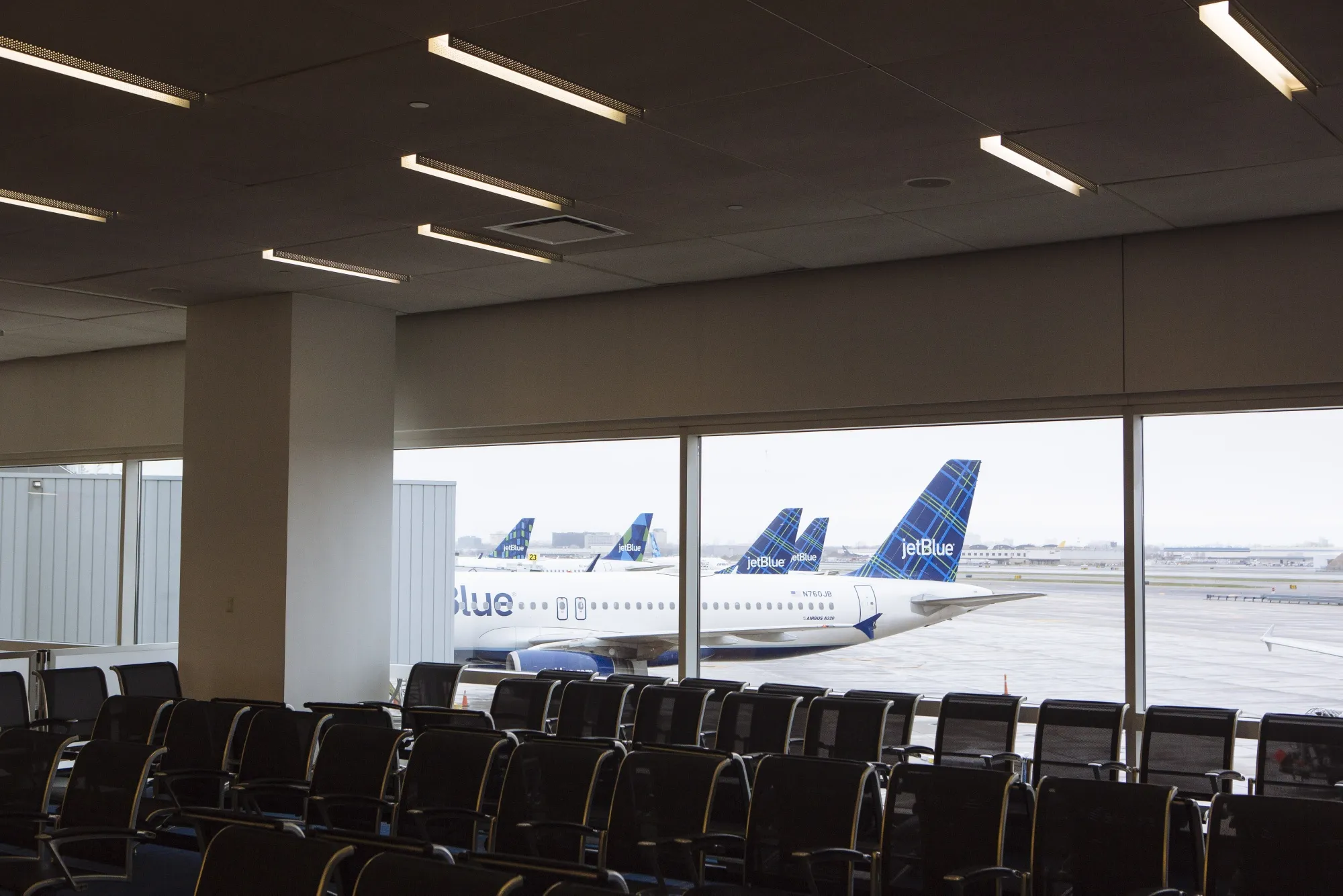 JetBlue planes sit at gates behind empty rows of chairs at JFK Airport.
