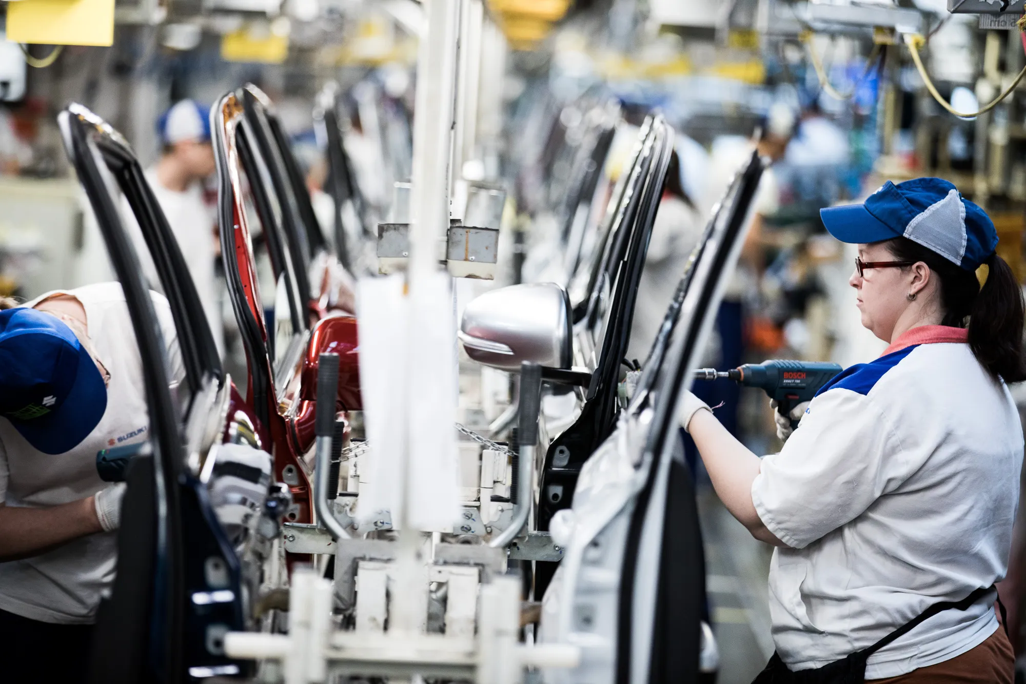 A female employee, right, works on an automobile door panel on the production line inside the Suzuki Motor Corp. plant in Esztergom, Hungary.