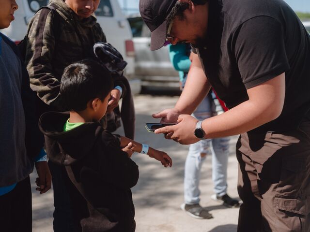 A volunteer scans the barcode on a wristband of a child migrant before boarding a bus to New York.