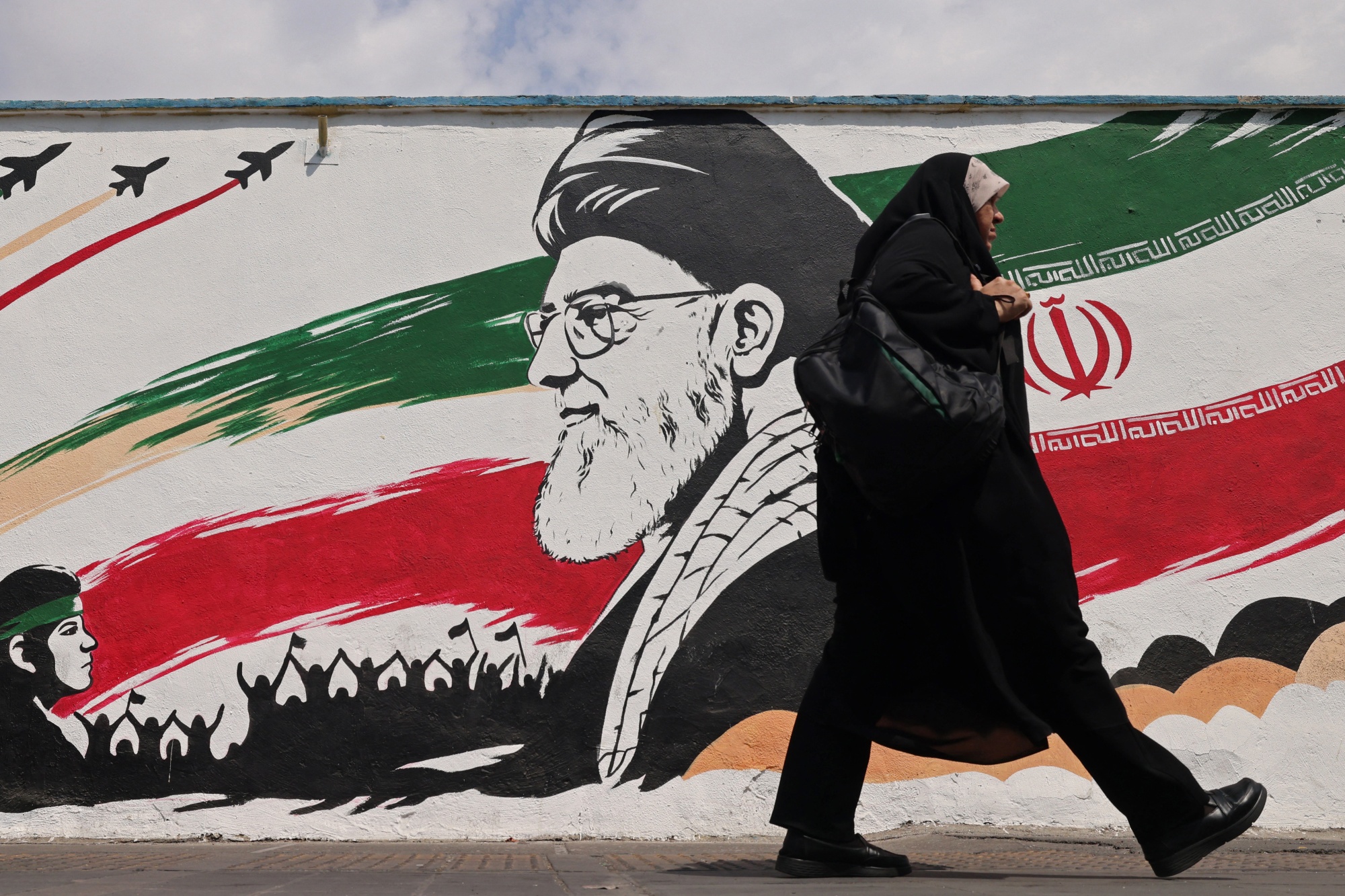 A woman walks past a wall mural of Iran’s slain supreme leader 