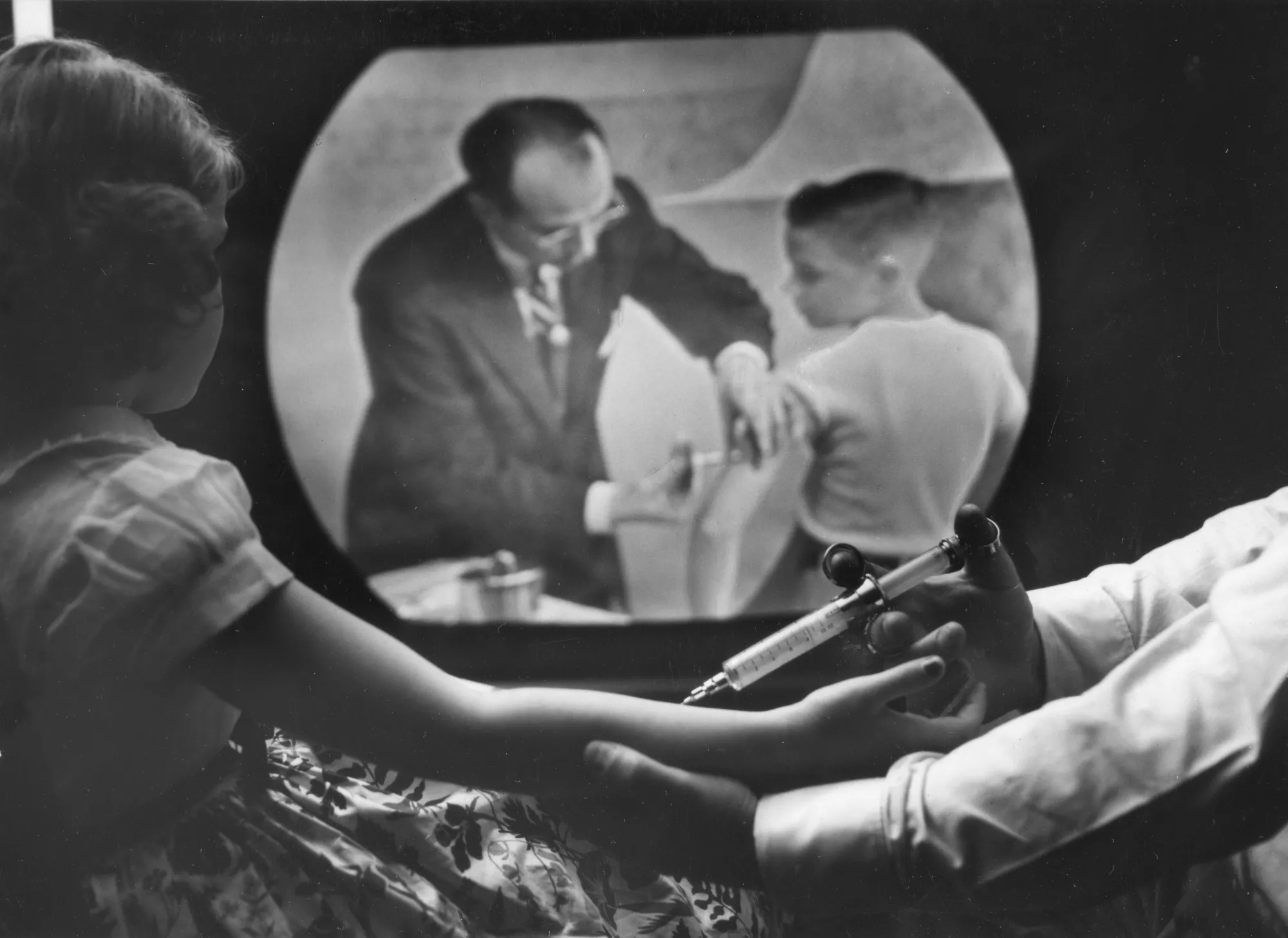 An&nbsp;eight-year-old girl receives the&nbsp;polio vaccine. On the television, Jonas Salk inoculates a&nbsp;boy in a training telecast for physicians and scientists April 12, 1955.