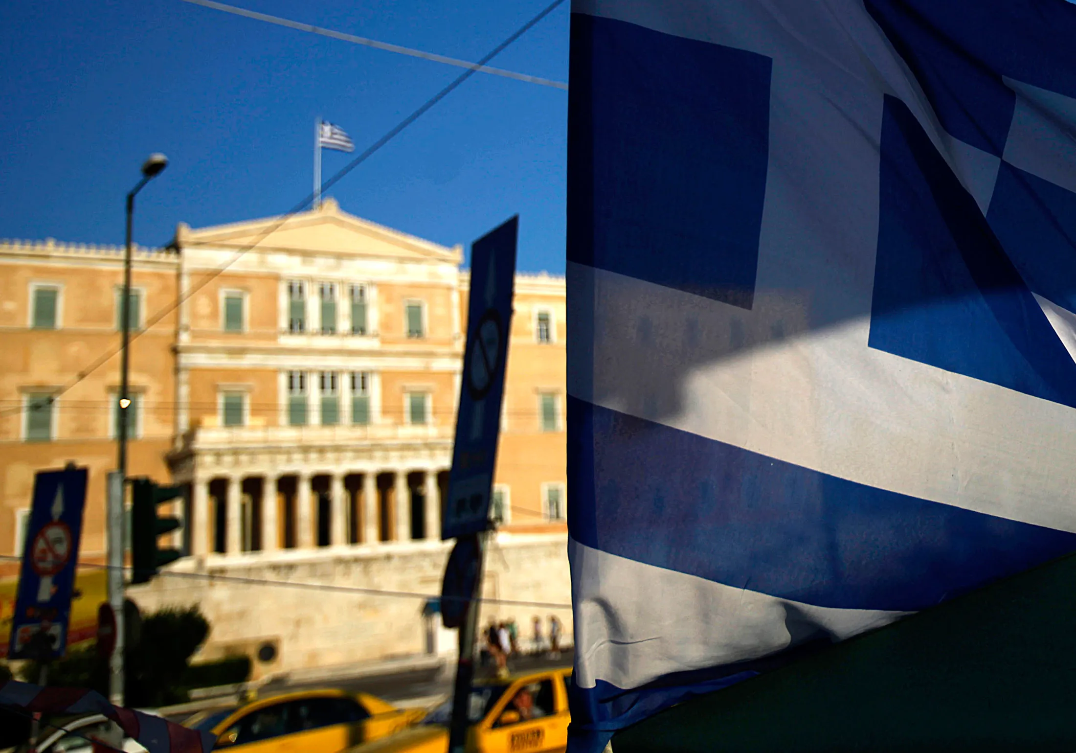 The national flag of Greece flies above the parliament building in Athens, Greece.
