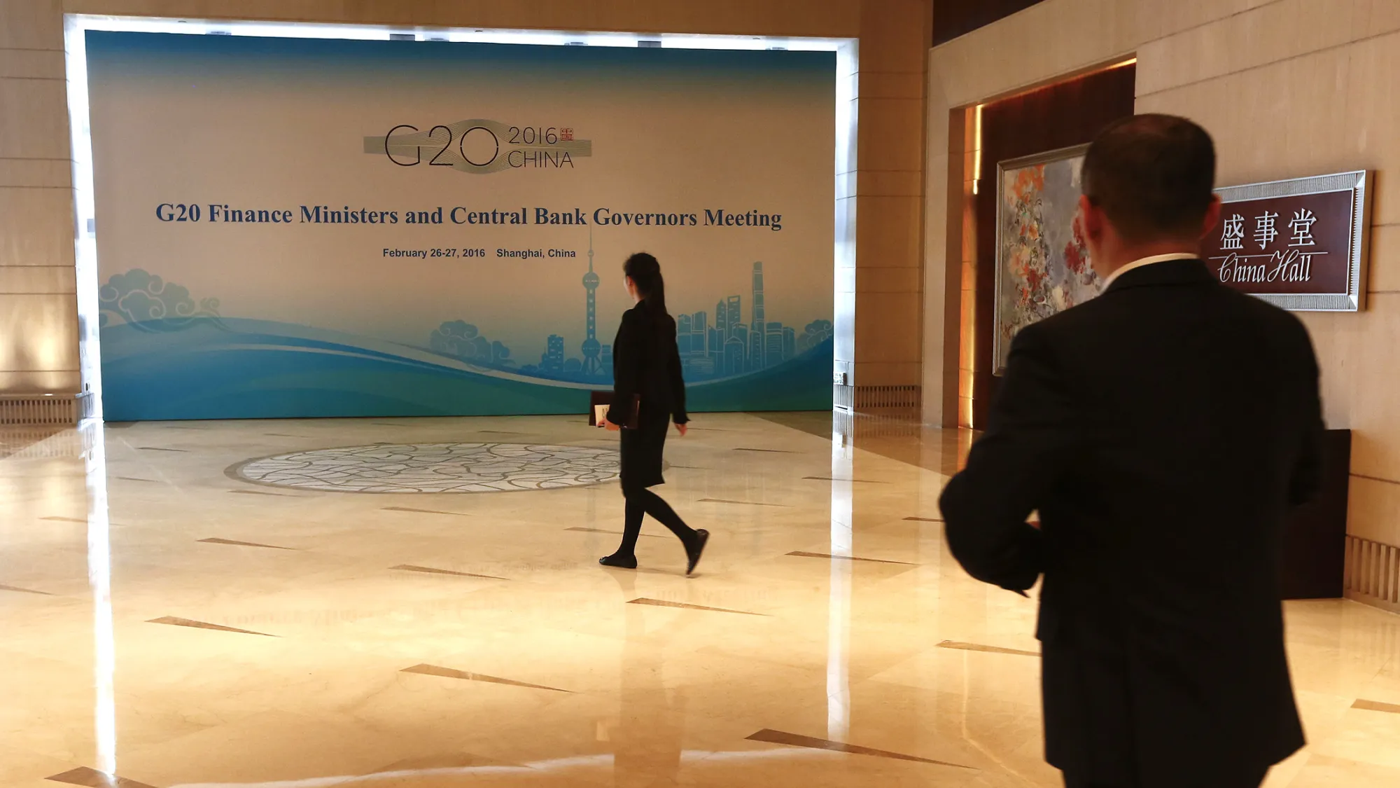 Chinese event staff walk past a sign one day before the start of the G20 Finance Ministers and Central Bank Governors Meeting at the Pudong Shangri-la Hotel in Shanghai on February 25, 2016.
