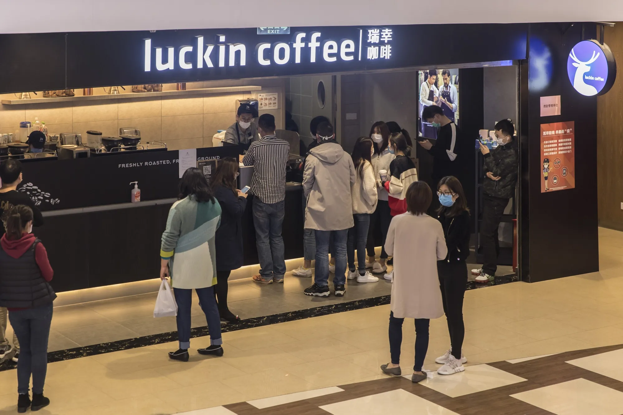 People wearing protective masks wait at a Luckin Coffee Inc. outlet in Shanghai.